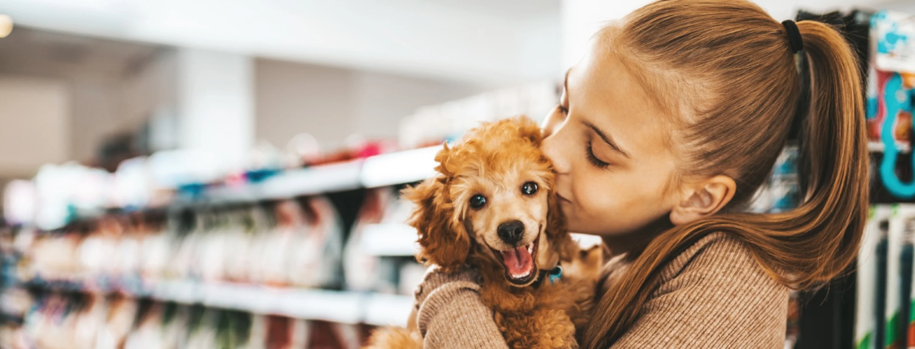 Girl holding and kissing a small dog while in a store